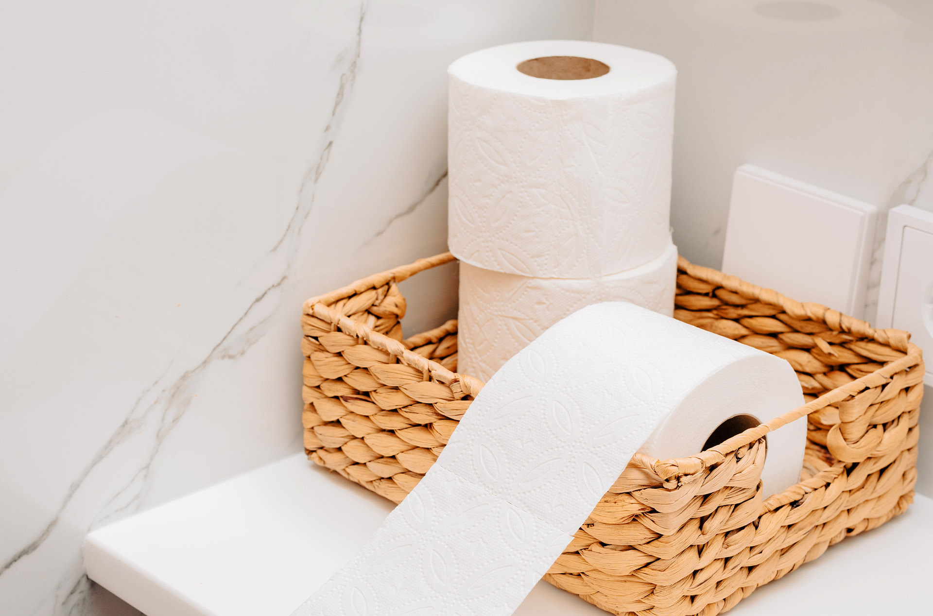 Recycled toilet paper rolls in a wicker basket—bulk-packed bathroom supplies for Airbnb hosts.