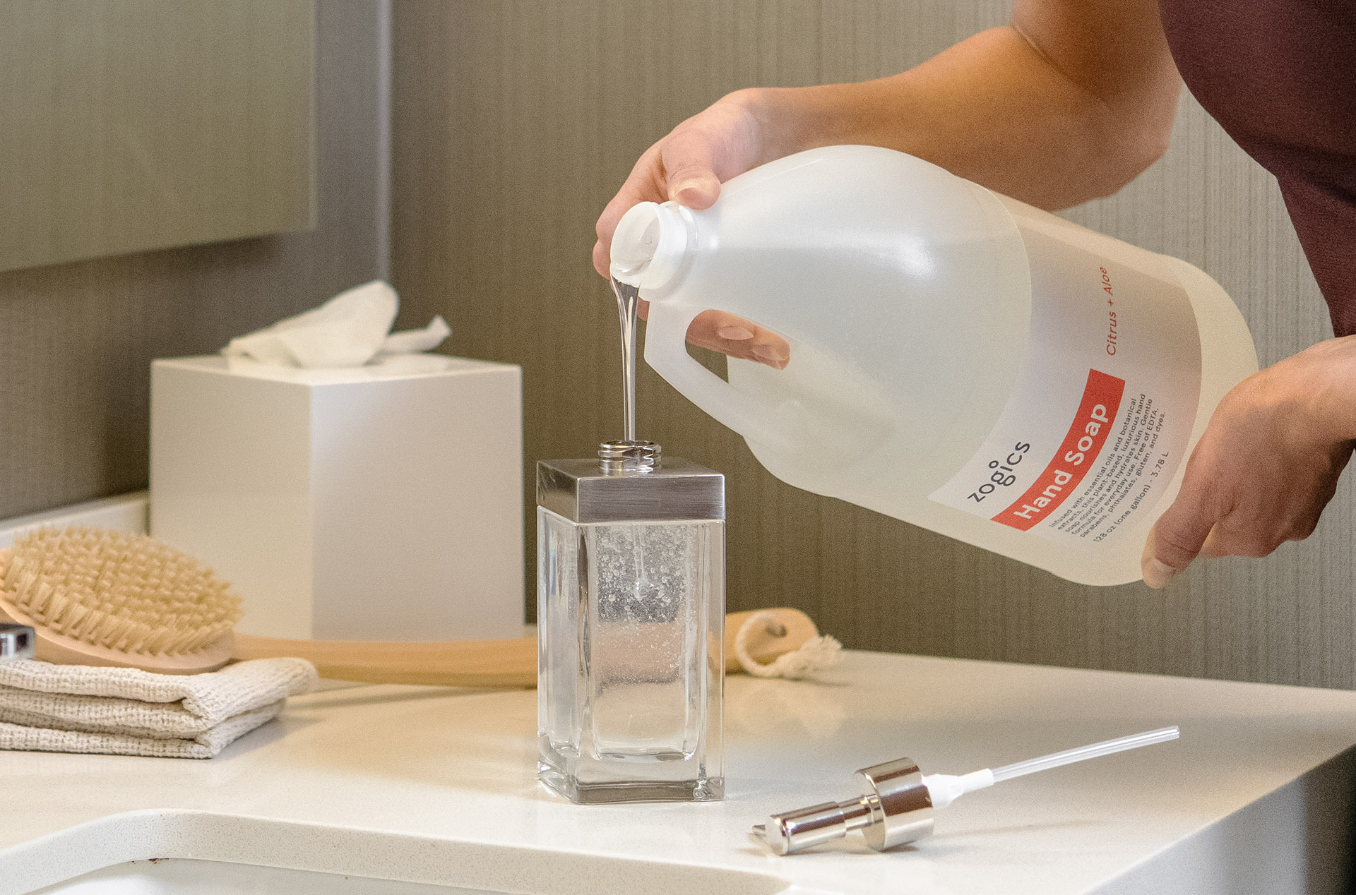 Refilling a clear liquid hand soap dispenser with Zogics Citrus + Aloe in a tidy Airbnb bathroom