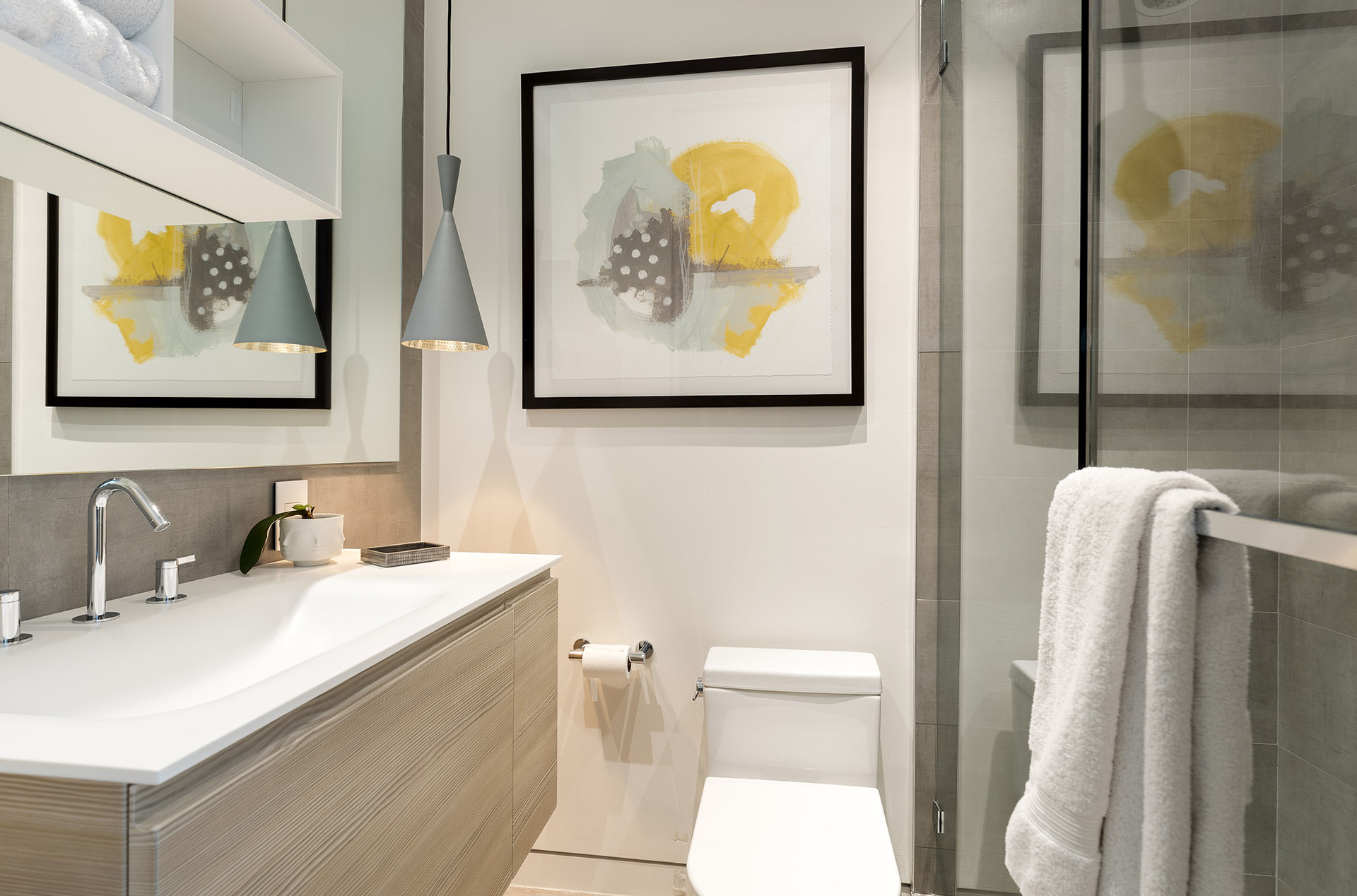 Modern Airbnb bathroom with framed artwork, layered lighting, glass shower, and white towels